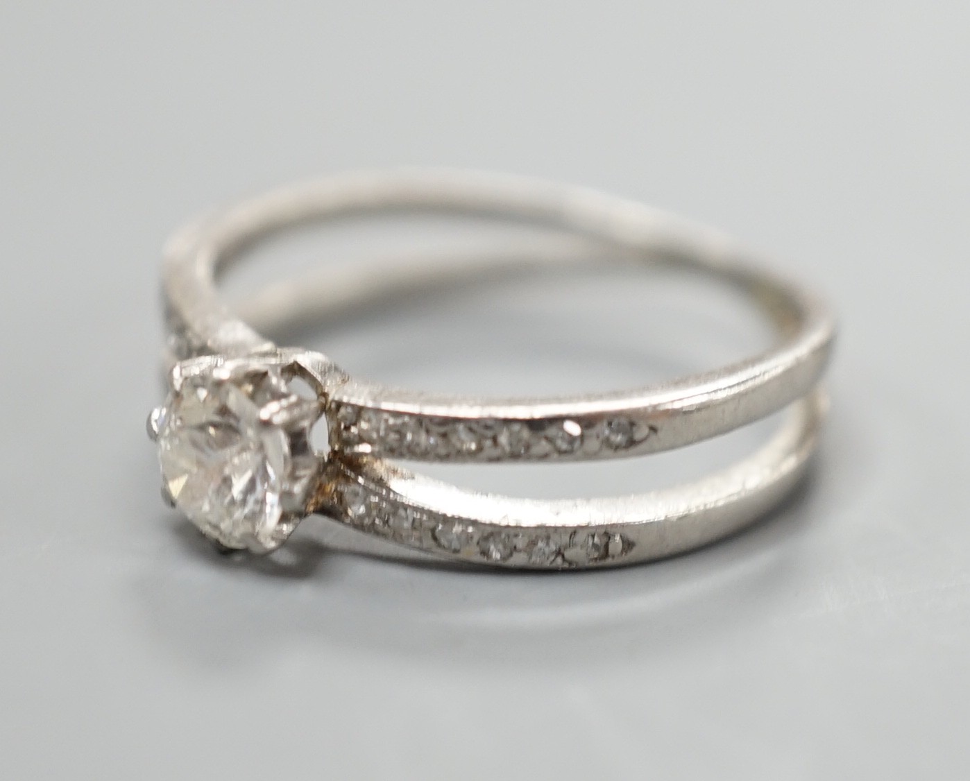 A modern white metal and single stone diamond ring, with diamond chip set crossover shoulders, size K, gross weight 3.3 grams.